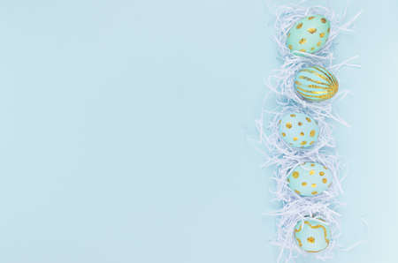 Modern easter eggs with golden design in white nest as border on blue background, top view.の写真素材
