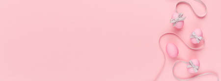Cute and naivety easter banner with pink eggs and wavy gray ribbons on pastel pink backdrop.の写真素材