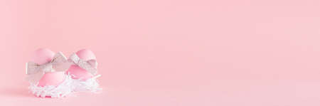 Sweet easter banner with pink easter eggs with silver bow in white nest on pastel pink backgroundの写真素材