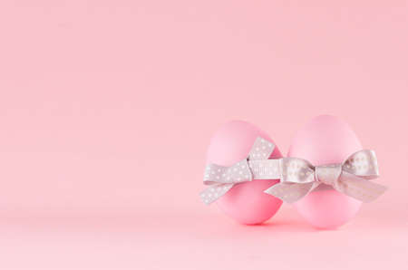 Exquisite soft pink easter eggs with silver bow standing on pastel pink background.の写真素材
