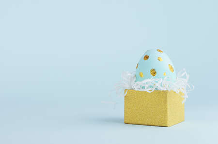 Modern easter egg with golden dots in golden gift box on blue background, copy space.の写真素材