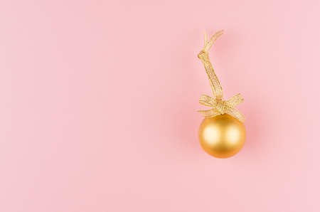 Christmas elegant background - golden sparkling glossy ball with ribbon on soft light pastel pink background, copy space, top view.の写真素材
