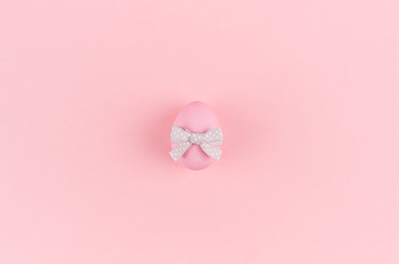 Pink easter egg with gray ribbon standing on pastel pink background, copy space.の写真素材