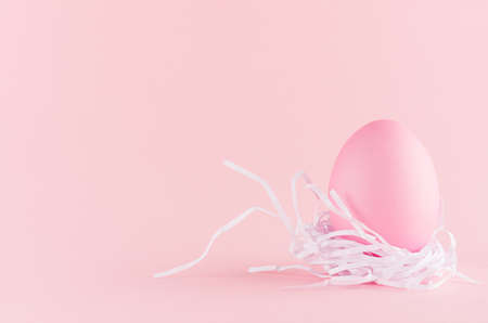 Gentle and girlish easter background - easter egg in white nest standing on pastel pink backdrop, copy space.の写真素材