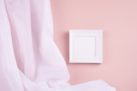 Delicate home decor with blank square photo frame hanging on pastel pink wall, flow of silk curtain. Mock up for portfolio, design or text.の写真素材