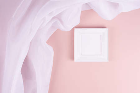 Soft pastel pink interior with blank square photo frame and folded white silk curtain on wall....