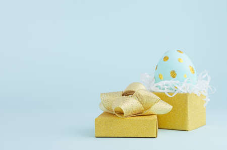 Blue easter egg with gold glitter dots in golden gift box on blue background, copy space.の写真素材