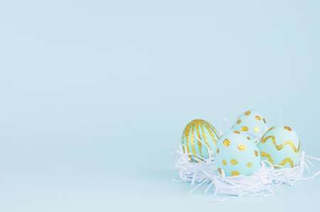 Bright easter background - blue eggs with golden design in white nest on blue backdrop, copy space.