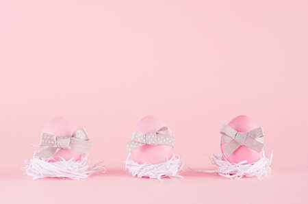 Fashion easter background - pink eggs with gray bows in white nest standing in row on pastel pink...