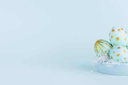 Handmade blue easter eggs with golden glitter design on bowl on blue background, closeup.の写真素材