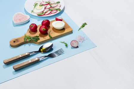 Spring fresh salad of radish, arugula and eggs, ingredients and cooking on blue background with...