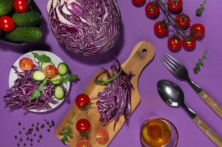 Cooking of fresh summer vegetable salad with red cabbage, cherry tomato, cucumber, arugula and oil with shadow in sunny day on purple background.の写真素材