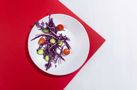 Fresh summer vegetable salad with red cabbage, cherry tomato, cucumber with shadow in sunny day on red color, white wood table, top view.の写真素材