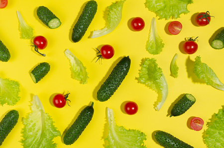 Food colorful vegetables pattern - cherry tomatoes, green gherkin cucumber, salad leaves in hard light with shadow on yellow background, flat lay.の写真素材