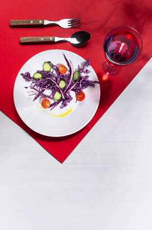 Raw healthy salad with purple cabbage, red tomatoes, cucumber, drink in hard light with shadow on modern geometric red color, white wood background, vertical.の写真素材