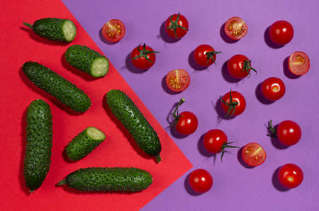 Bright cherry tomatoes, green gherkin cucumber in hard light with shadow on red and violet background, flat lay, food colorful pattern.の写真素材