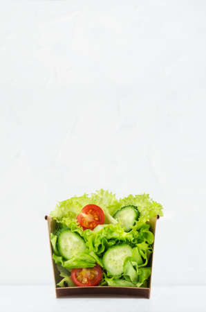 Wellness take away appetizer - fresh healthy salad of raw vegetables in craft package for fast food with showing ingredients inside on soft light white background, vertical.の写真素材