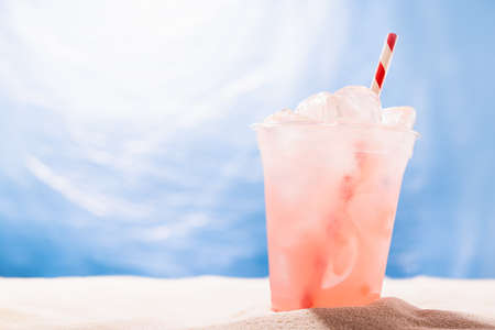Fresh strawberry beverage with ice, straw in plastic glass on sandy tropical beach with sea view, copy space. Vacation, relax on coast.の写真素材