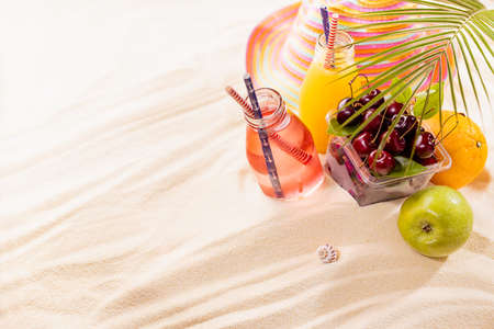 Healthy summer beach vacation on ocean coast - cold juices in glass bottles, fresh cherries, orange,...