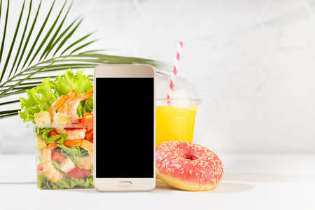 Wellness summer food set of orange juice, pink donut, tropical shrimp salad in box, blank phone in...