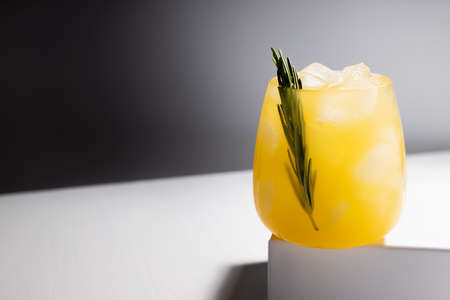 Fresh misted orange alcohol cocktail in glass with ice, green rosemary twig on podium in sunlight with shadows in elegant minimal black and white interior.の写真素材