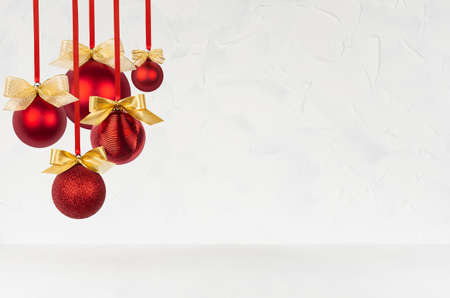 New Year background in simple style with shiny red balls with golden bows hanging on ribbon as bunch on soft light white wall and wood table, for design of poster, flyer, card, brochure, copy space.の写真素材