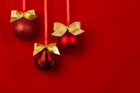 Shimmer balls with golden bows hang on ribbons in row on saturated red backdrop, copy space. Rich christmas background in modern style for design of poster, flyer, card, brochure.の写真素材