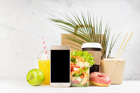 Fitness food set of coffee, juice, shrimp salad, noodles in box, donut, packet, blank phone in white...