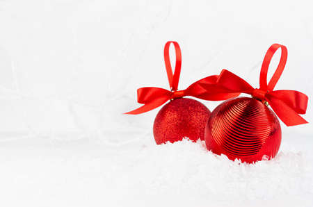 Bright christmas background - two elegant glossy glitter red balls with satin ribbon closeup in decorative fairy white winter forest, frosty branches, snow, copy space. Festive New Year background.の写真素材