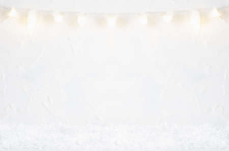 Christmas glowing garland defocused hang on soft light wall and white fluffy snow as abstract winter festive background.の写真素材