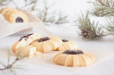Christmas biscuits cooking with jam on white wood table with pine branches in soft light white interior, closeup.の写真素材