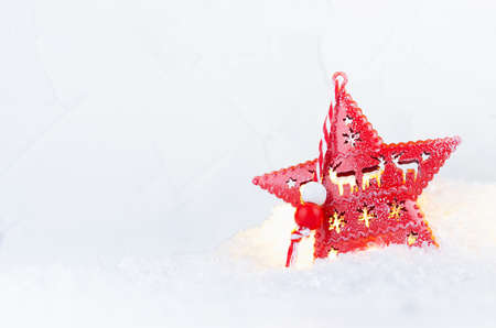 Christmas decoration - red star with festive burning lights inside, closeup, in fluffy white snow, closeup.の写真素材