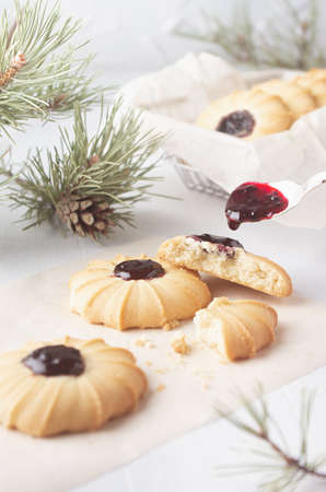 Cooking sweet traditional christmas crumbly biscuits in silver basket with dripping jam from spoon on white wood table with green pine branches, vertical, closeup.の写真素材