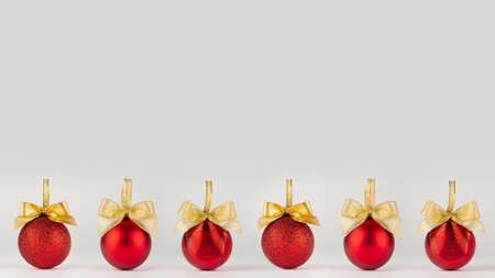 Bright New Year background - shimmer red balls with gold bows stand in row as pattern border on soft light white table in minimal style, copy space. For design of poster, flyer, card, brochure.の写真素材