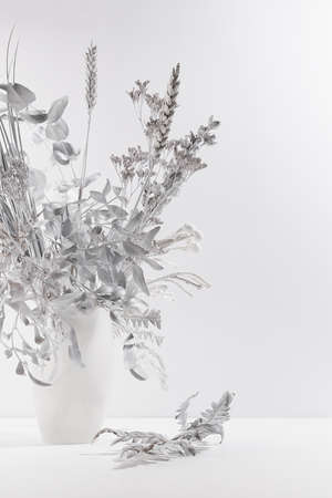 Winter frost white bouquet of dried plant - eucalyptus, reed, fern and flowers in vase on wood table as festive delicate modern home decor for soft light interior, copy space, vertical.の写真素材