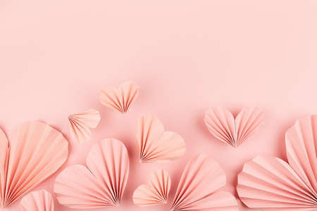 Hearts background for Valentines day, wedding - beautiful tender pink paper ribbed hearts in simple origami style soar on pastel pink color as footer border, copy space. Love backdrop for card, text.の写真素材