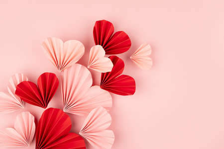 Bright and passion Valentines day background - curved flow of pink and red paper ribbed hearts flying on soft light pastel pink background as border with copy space, top view.の写真素材