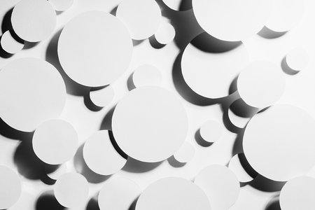 White paper circles different size as mess swarm random abstract pattern in hard light with contrast black strict shadows, top view. Contemporary simple stable bright abstract background.の写真素材