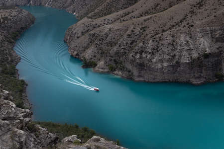 Majestic colorful turquoise blue river, red speed boat float with curved white path and waves on water among high steep mountain slopes. mountain landscape. Hiking, tourism, travel in wild outdoor.の写真素材