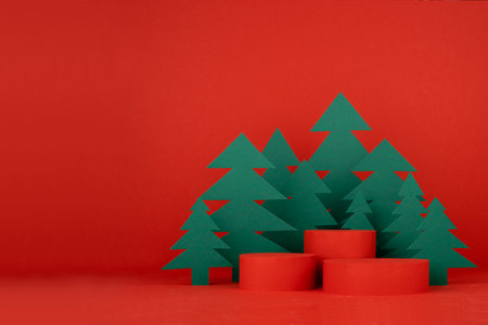 Christmas art three cylinder podiums and red stage for presentation gifts, cosmetic products, goods, green paper spruces in cartoon style, copy space. New year template for advertising, design.の写真素材