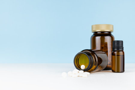 Medical and treatment background with different amber glass bottles with white pills and vitamin capsules for prevention and therapy disease, sickness, ache on white table, blue wall, copy space.の写真素材
