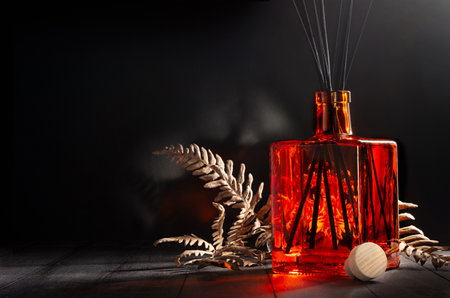 Home decor background with elegant orange glass aromatic diffuser as bottle with black sticks in darkness on black wood table, copy space. Cozy and relaxing atmosphere of interior at winter night.の写真素材
