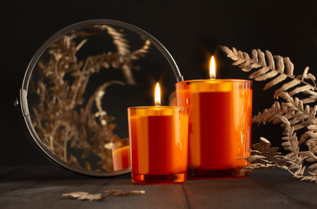 Atmosphere burning orange candles in orange glass with dry leaves, round mirror as elegant home...