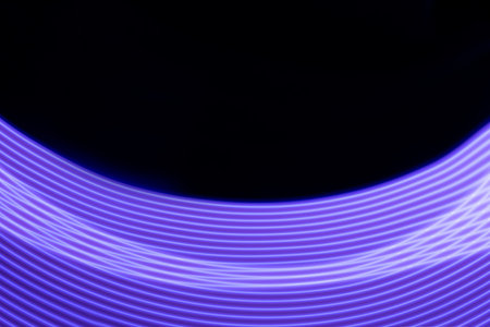Violet shining neon smooth stripes of light on black background. Abstract background with energy line in motion, light painting in futuristic style.の写真素材