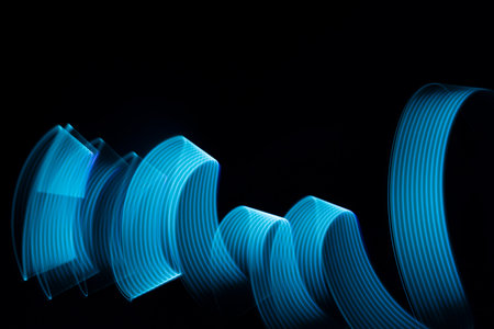 Blue neon curved wave of light as curls or swirl with smooth stripes on black background. Abstract...