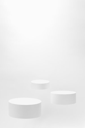Abstract scene - three round white tilt podiums for cosmetic products mockup, fly on white background. For presentation skin care products, gifts, goods, advertising, showing, sale in minimal style.の写真素材