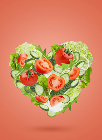 Healthy fresh vegetables as heart shape. Organic vegetable salad ingredients - tomatoes, green cucumbers, mixed greens, chinese cabbage fly on red background. Vegetarian diet food for detox eating.の写真素材