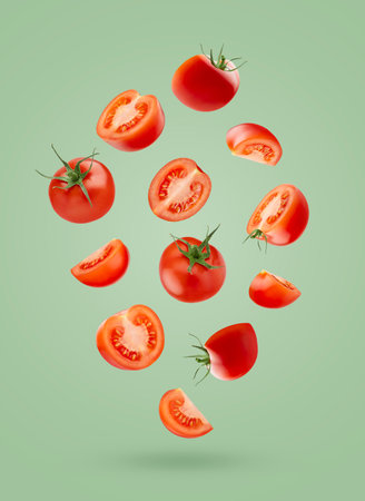 Juicy red cherry tomatoes - perfect round, whole and slices fly as flow on green background as art composition. Wholesome and vitamin ingredient for salads, healthy dietary menus.の写真素材