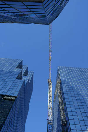 Skyscraper construction crane surrounded by glass towersの写真素材