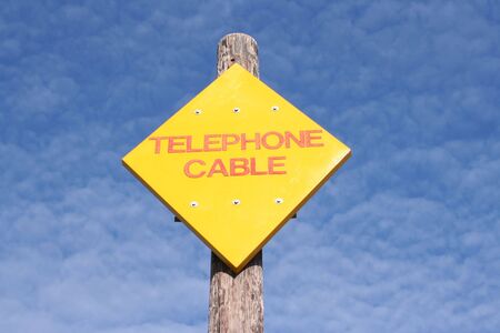 bright yellow telephone cable sign against blue sky